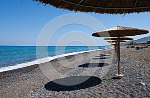 Tropical beach umbrellas providing sunshade for swimmers at an empty beach. Summer vacations.