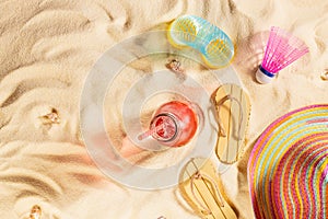 Tropical beach vacation background - fresh cold pink drink with straw, sun hat, slippers, slinky toy on white sand, top view.