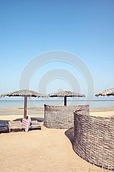 Tropical beach with wooden umbrellas, sun beds and wind screens, color toning applied