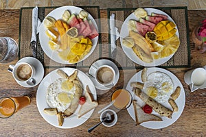 Tropical breakfast of fruit, coffee and scrambled eggs and banana pancake for two on the beach near sea. Top view, table setting