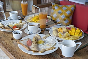 Tropical breakfast of fruit, coffee and scrambled eggs and banana pancake for two on the beach near sea. Top view, table setting