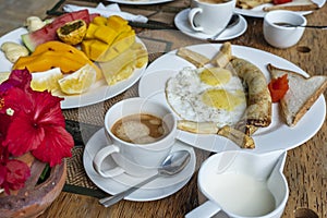 Tropical breakfast of fruit, coffee and scrambled eggs and banana pancake for two on the beach near sea. Top view, table setting