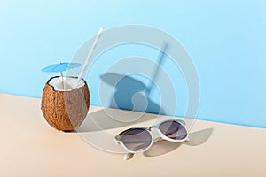 Tropical cocktail in coconut with straw and an umbrella, on paper blue and yellow background. The concept of relaxation, summer