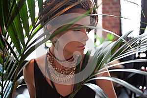 Tropical flavor. Close-up portrait of beautiful, woman with large jewels and afro braid, surrounded by tropical plants. photo