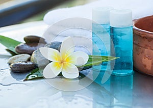 Tropical flower, bowl of water, dark stones, towel and cream tube. Body care and spa concept