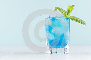 Tropical fresh alcohol cocktail with blue curacao liqueur, ice cube, green mint in frozen shot glass on soft light white.
