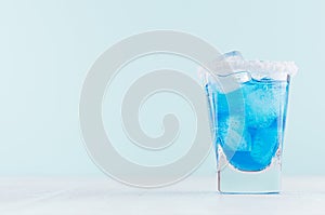 Tropical fresh alcohol cocktail with blue curacao liqueur, ice cube, salt rim in frozen shot glass on soft light white.