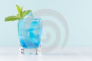 Tropical fresh cocktail with blue curacao liqueur, ice cube, sugar rim, green mint in frozen shot glass on soft light white.