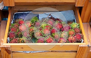 Tropical fruit rambutan in wooden box. Exotic fruit on organic market in Asian village. Fruit season in Asia