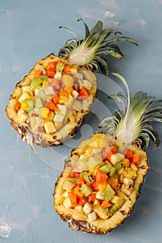 Tropical fruit salad in pineapple halves on a light blue background, Closeup, vertical orientation
