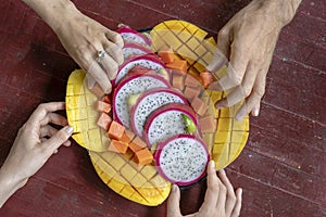 Tropical fruits assortment on a plate and people hands, close up. Yummy dessert, close up. Mango, papaya, pitahaya and hands, top