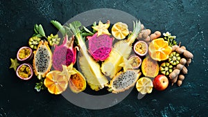 Tropical fruits - passion fruit, pineapple, dragon fruit, kiwi and cactus on a black background. Top view.