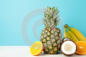 Tropical fruits. Pineapple, coconut, orange and banana on blue background. Space for text