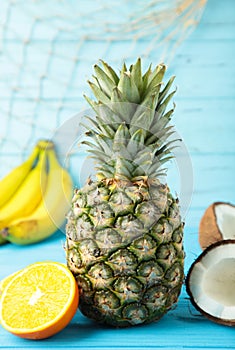 Tropical fruits. Pineapple, coconut, orange and banana on blue background. Vertical photo