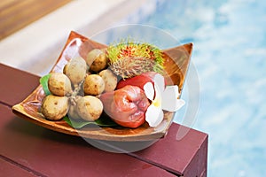 Tropical fruits in soft focus on wooden tray near swimming pool