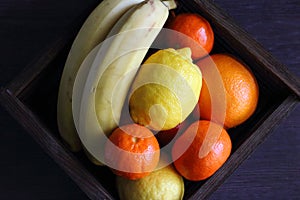Tropical fruits in wooden basket on table top view. Juicy mandarins, orange, lemon and banana. Sweet vitamin ripe fruits.
