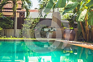Tropical garden at modern villa with swimming pool among palm trees and Asian ornamental elements