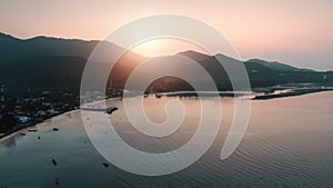 Tropical island bay at pink sunrise. Aerial panorama over beach pier, coastline village, calm ocean