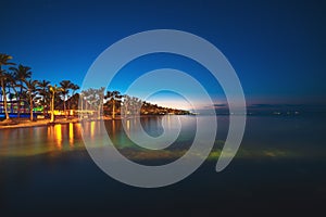 Tropical island at night. Palm trees silhouettes and lights on resort beach