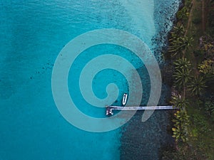 Tropical island and wooden pier with boat, top down view