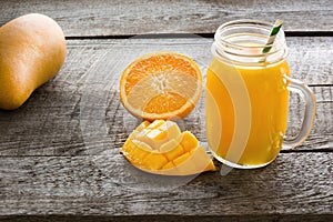 Tropical juice of mango, orange, banans fruit in jar with straw on wooden board.