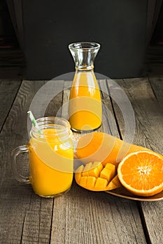 Tropical juice of mango, orange, banans fruit in jar with straw on wooden board.