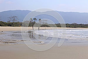 Tropical landscape of a beach with calm water. Green vegetation in the background and blue mountains far away