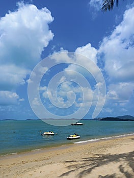 Tropical landscape. Blue sky, white clouds, beach, warm ocean and speedboats on it. photo