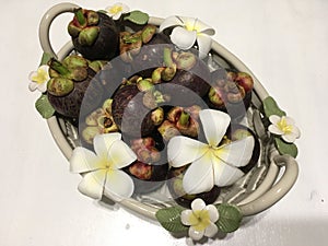 Tropical mangosteen fruits in ceramic basket, decorated with frangipani flowers