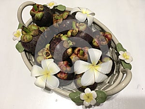 Tropical mangosteen fruits in ceramic basket, decorated with frangipani flowers photo