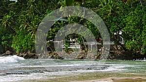 Tropical Mirissa beach lagoon, Sri Lanka, waves crash against rocks lush palm trees surround cabanas, secluded paradise