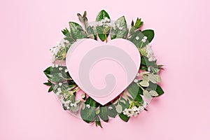 Tropical nature background with green leaves, white flowers and pink heart shaped paper for copy space. Top view. Flat lay.