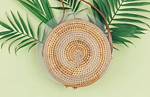 Tropical palm leaves, straw bag on a green background. Trendy tropical pattern. Fashion clothing and accessories. Flat lay. Summer