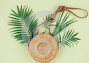 Tropical palm leaves, straw bag, on pastel green background. Trendy tropical pattern. Fashion clothing and accessories. Flat lay.