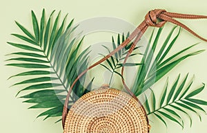 Tropical palm leaves, straw bag, on pastel green background. Trendy tropical pattern. Fashion clothing and accessories. Flat lay