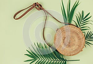 Tropical palm leaves, straw bag,  on pastel green background. Trendy tropical pattern. Fashion clothing and accessories. Flat lay.