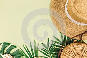 Tropical palm leaves, straw hat on a green background. Trendy tropical pattern. Fashion clothing and accessories. Flat lay. Summer