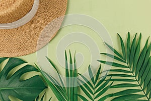 Tropical palm leaves, straw hat on pastel green background. Trendy tropical pattern.