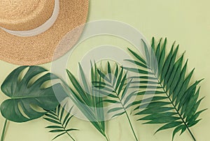 Tropical palm leaves, straw hat on pastel green background. Trendy tropical pattern. Fashion clothing and accessories. Flat lay