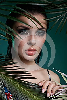 Tropical portrait sexy woman in leaves palm tree. Bright green makeup, shadow of palm leaves on girl face. Beautiful makeup
