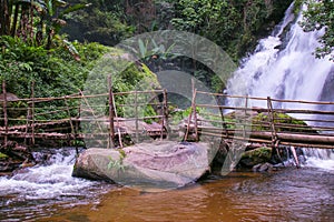 Tropical rain forest landscape with jungle plants, flowing water of Pha Dok Xu waterfall and bamboo bridge. Mae Klang Luang