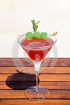 Tropical red cocktail with green sugar cherries on the wooden table at the beach and ocean