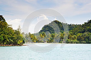 Tropical sea and sandy beach with palm trees and bungalows on the island on horizon at the Koh Chang island, Thailand.