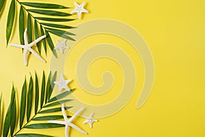 Tropical summer vacation concept with palm tree leaves and starfish on yellow background. Top view from above