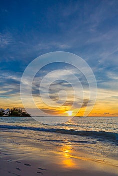 Tropical sunset with sun reflecting off the water and wet sand