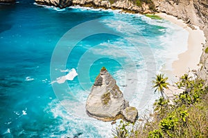 Tropical view of a beach with palms and rock in Nusa Penida, Indonesia.