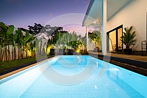 Tropical villa view with garden, swimming pool and open living room at sunset