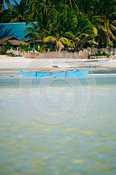 Tropical white sand beach with green palm trees and parked fishing boats in the sand. Exotic island paradise