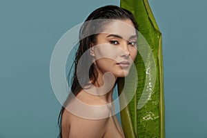 Tropical woman peeking out from behind exotic plant big leaf.