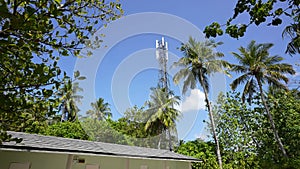 Tropical worker servicing cellular antenna in front of sunlight, drone view of telecommunication antenna system